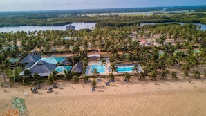 An aerial view of a resort with multiple buildings, a large pool, and a beach area with palm trees. - Casa Del Papa Resort & SPA (Ouidah)