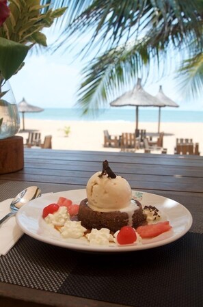 Un plato de postre con helado y frutas sobre una mesa en un lugar junto a la playa.
