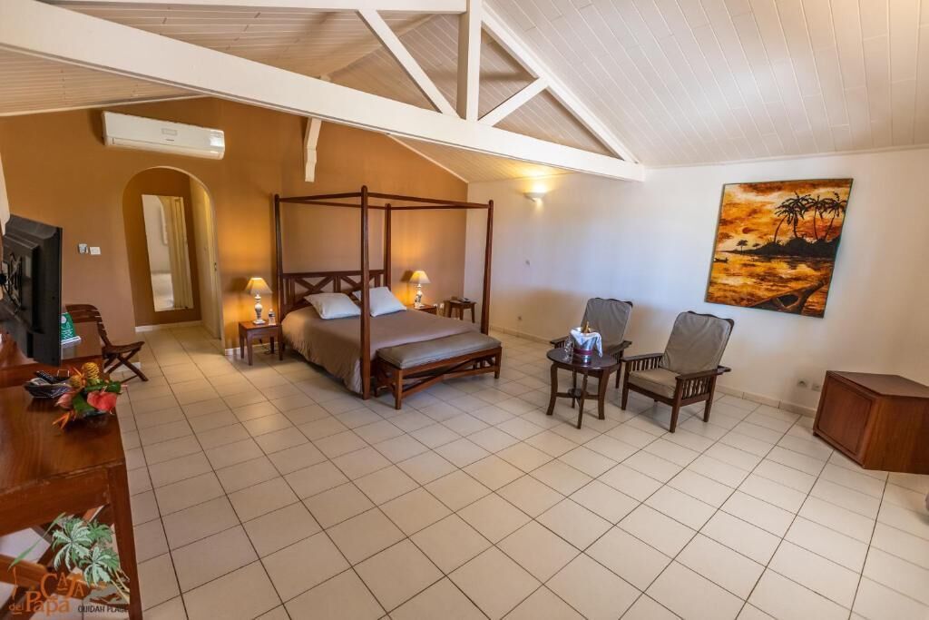A bedroom with a four-poster bed, a desk with a chair, a small table with a chair, and a painting on the wall.