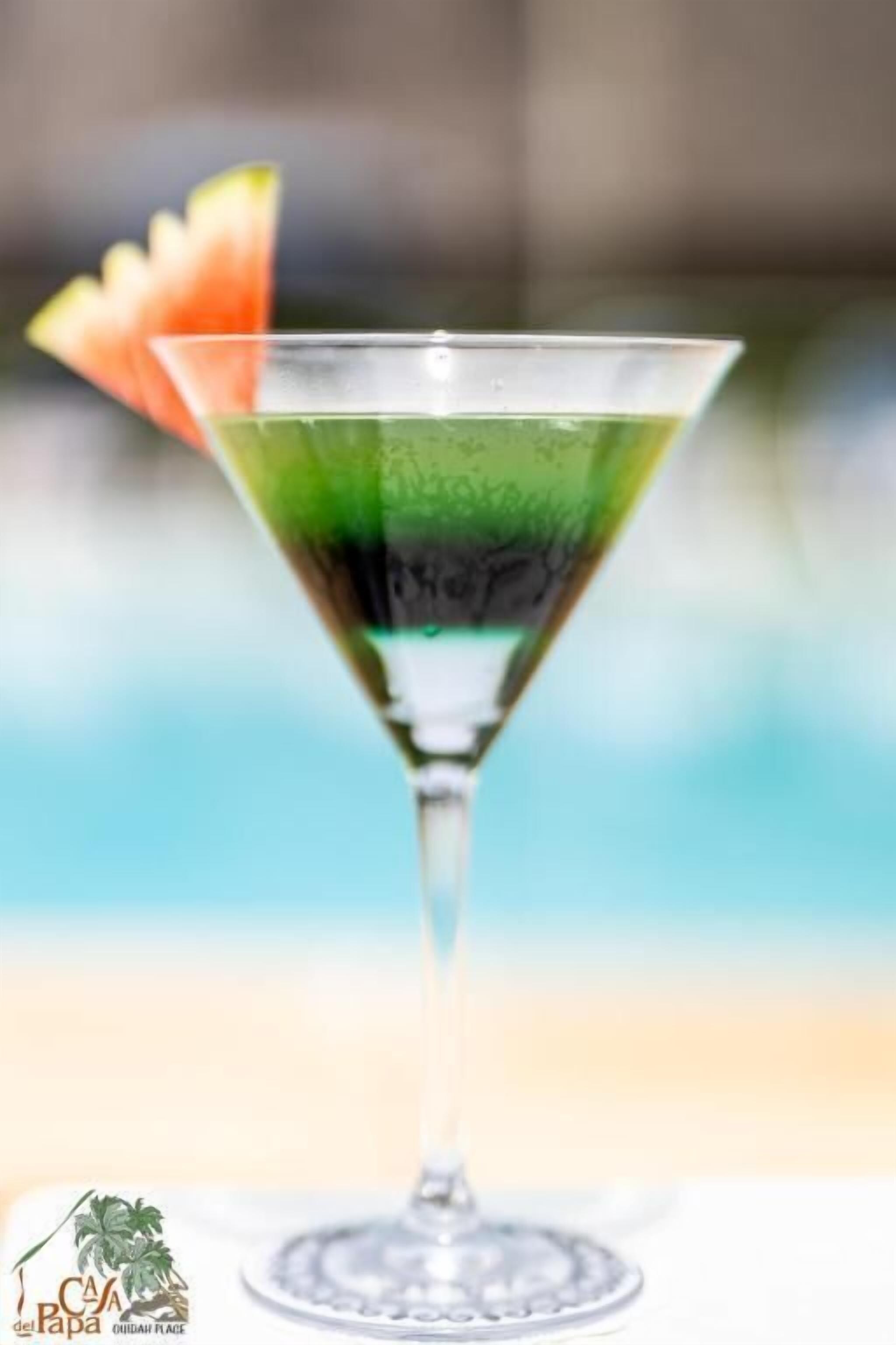 Un cóctel en una copa de martini, con una guarnición, sobre un fondo desenfocado.
