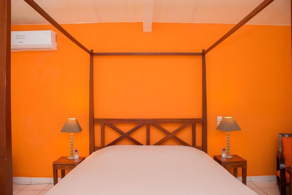 A room with an orange wall, a wooden headboard, and two bedside tables with lamps.