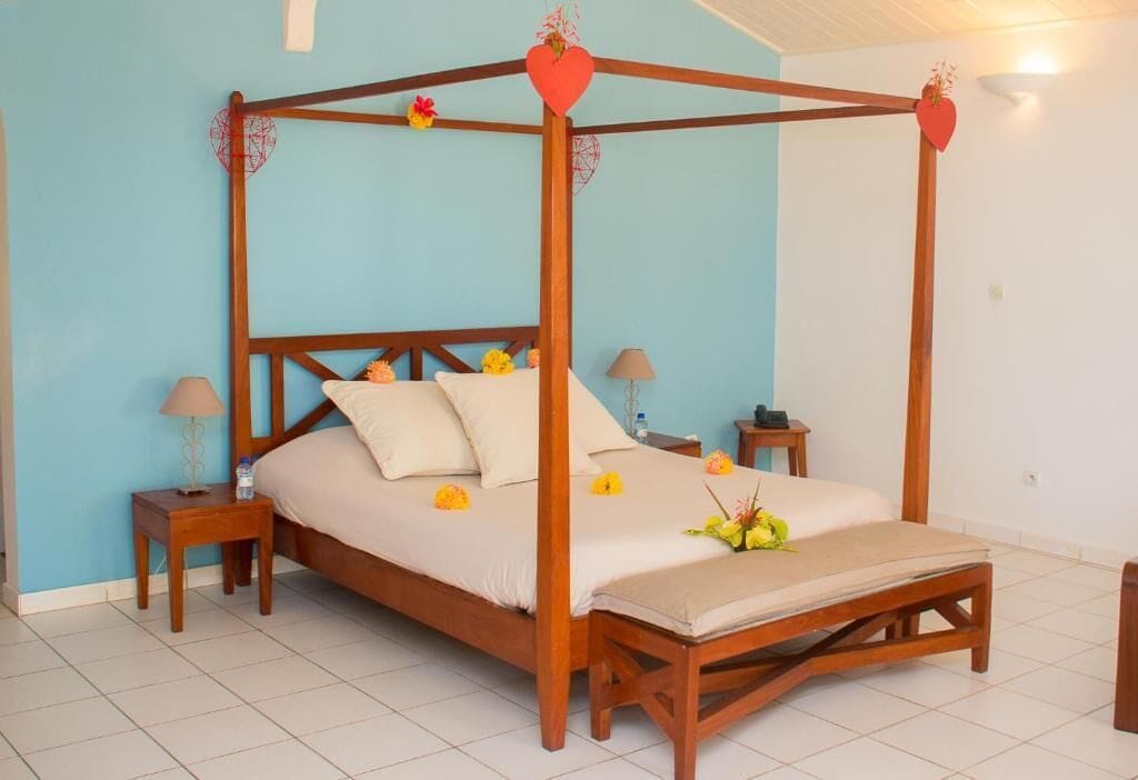 A four-poster bed with a wooden frame, white bedding, and decorative flowers. There are two bedside tables with lamps and a small table with a vase of flowers.