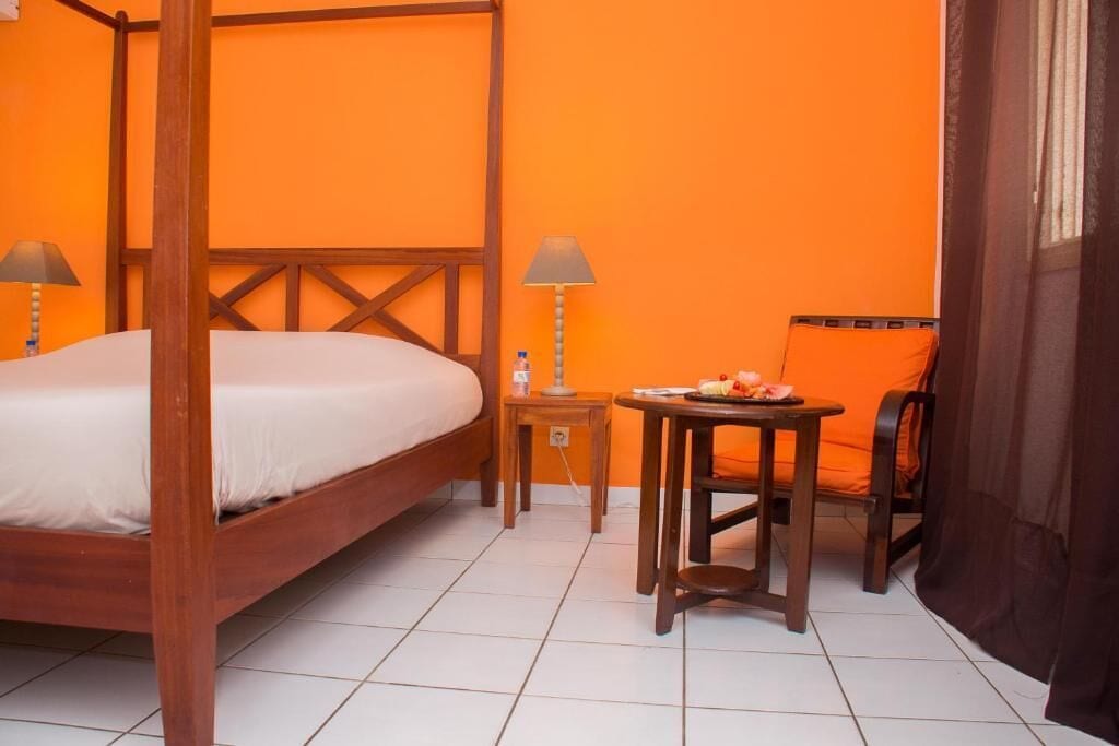 A room with a four-poster bed, two bedside tables with lamps, a small round table with a plate of fruit, and a chair.