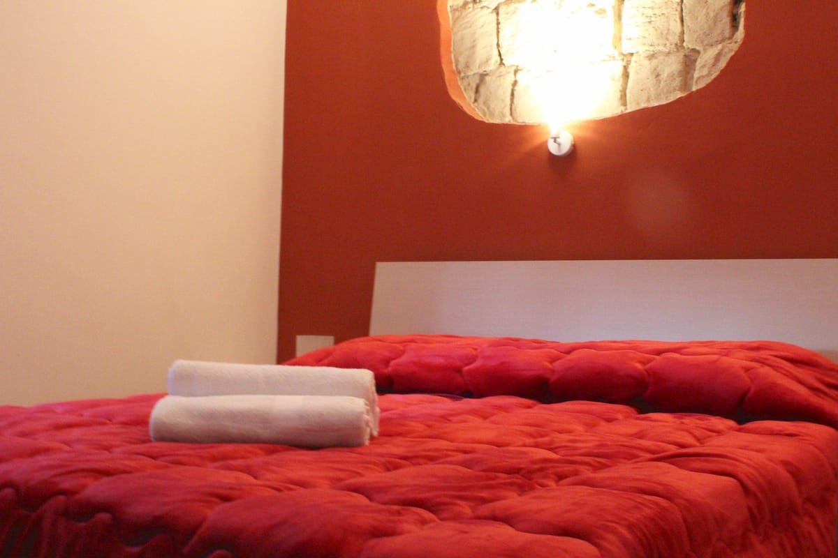 Una cama con una colcha roja y dos toallas blancas dobladas con cuidado.