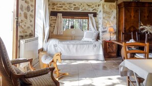 Un dormitorio con una cama, un sillón mecedor de madera, una mesa y una lámpara.