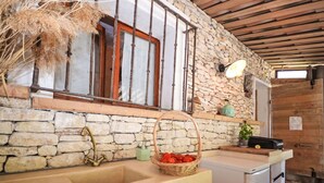 Una cocina rústica con pared de piedra, vigas de madera, un grifo antiguo y una cesta de tomates.