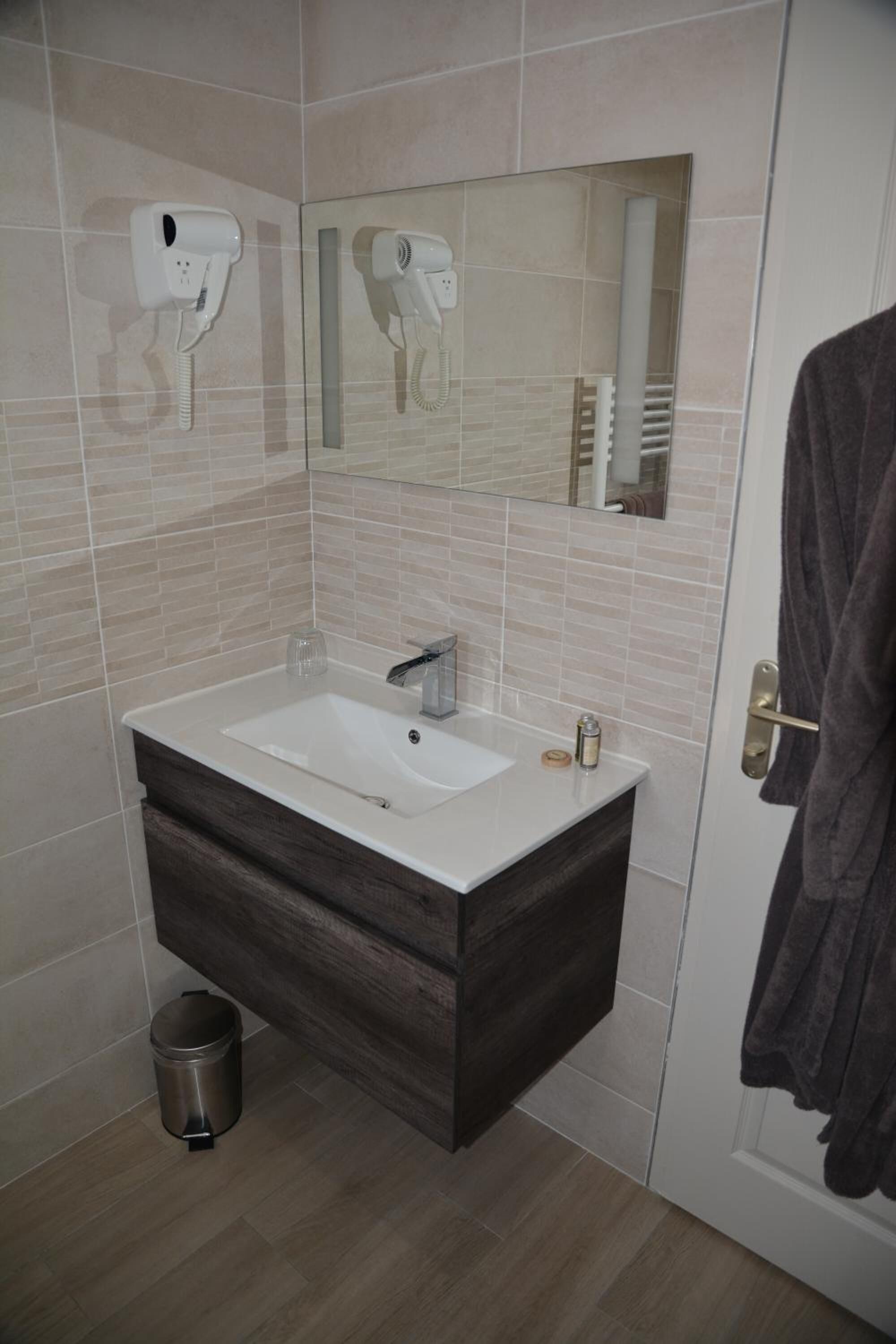 Un baño con lavamanos blanco, tocador de madera oscura, un espejo y un secador de pelo montado en la pared.
