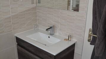 Un baño con lavamanos blanco, tocador de madera oscura, un espejo y un secador de pelo montado en la pared.