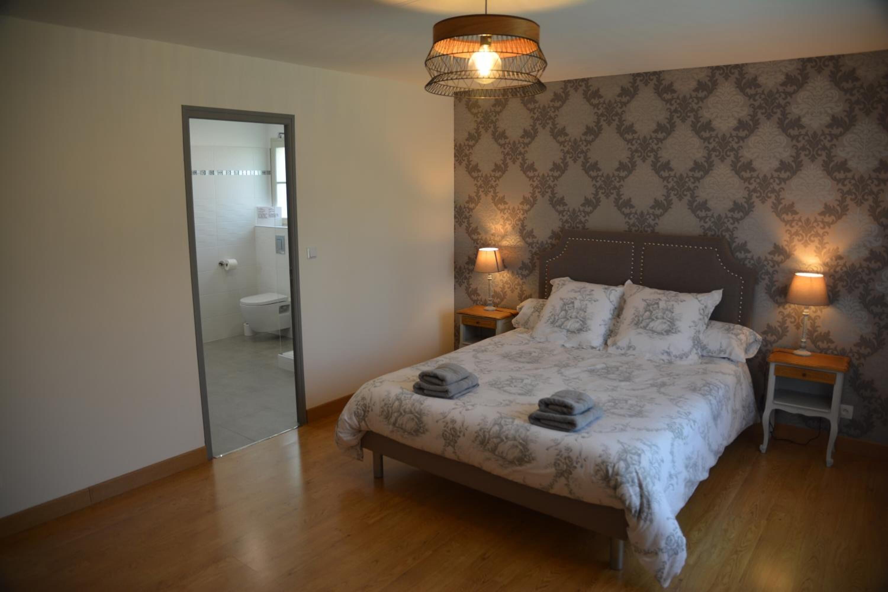 A bedroom with a large bed, two bedside tables with lamps, a mirror, and a patterned wallpaper.