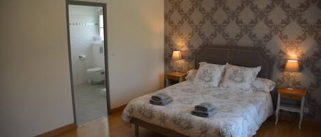 A bedroom with a large bed, two bedside tables with lamps, a mirror, and a patterned wallpaper.