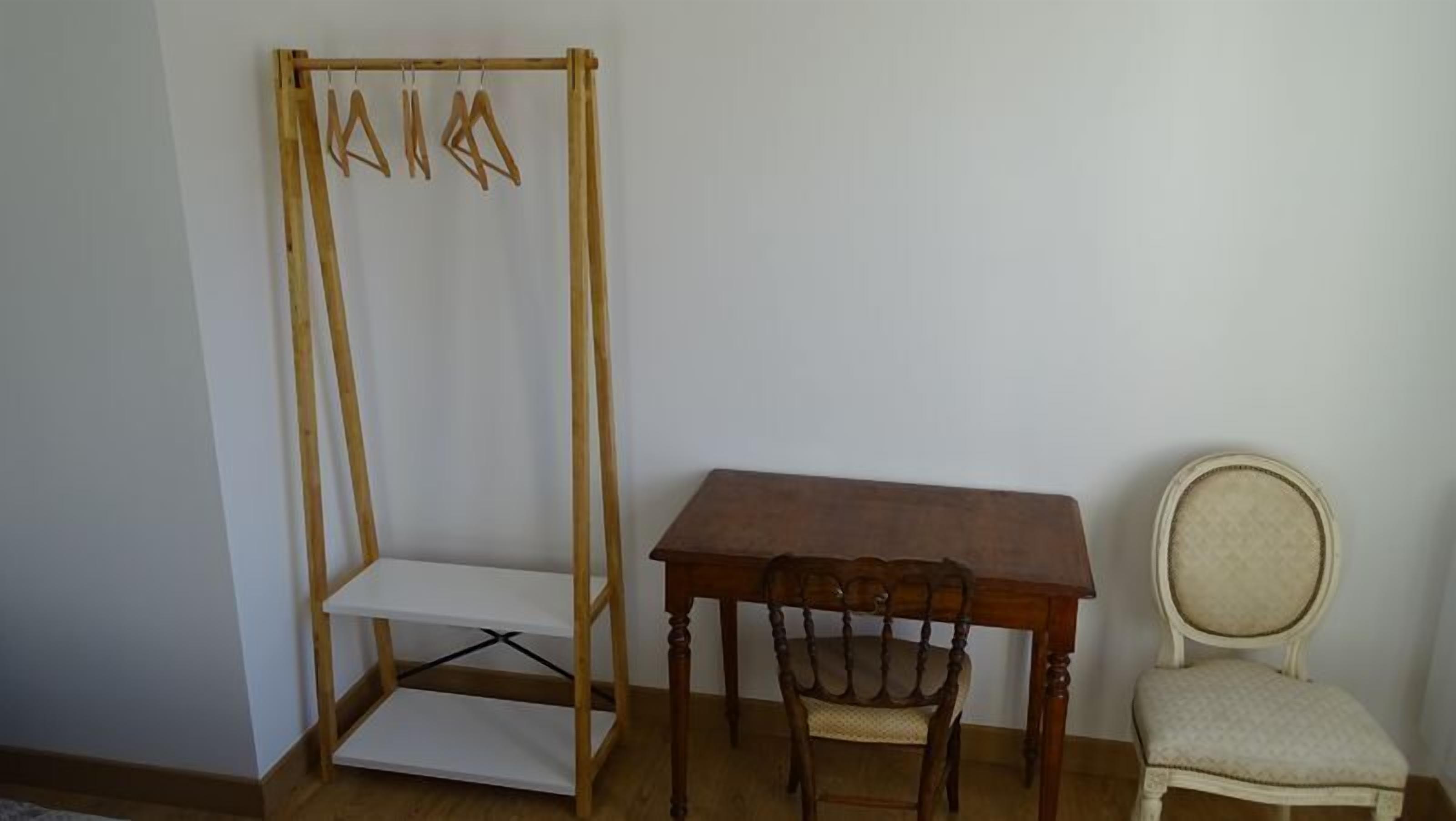 Una habitación con una mesa de madera, una silla y un perchero de madera con ganchos.