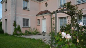 Un edificio rosa con una porta bianca, un giardino con rose e un pergolato in legno.