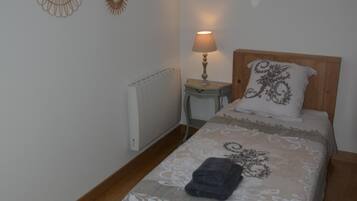A bedroom with a bed, a nightstand with a lamp, a radiator, and decorative wall mirrors.