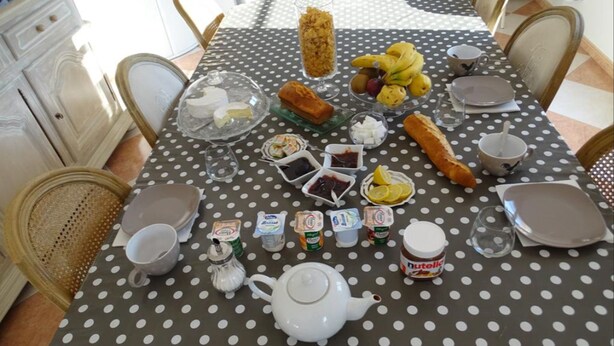 Un tavolo da pranzo apparecchiato con diversi cibi, tra cui pane, frutta e condimenti, su una tovaglia a pois.