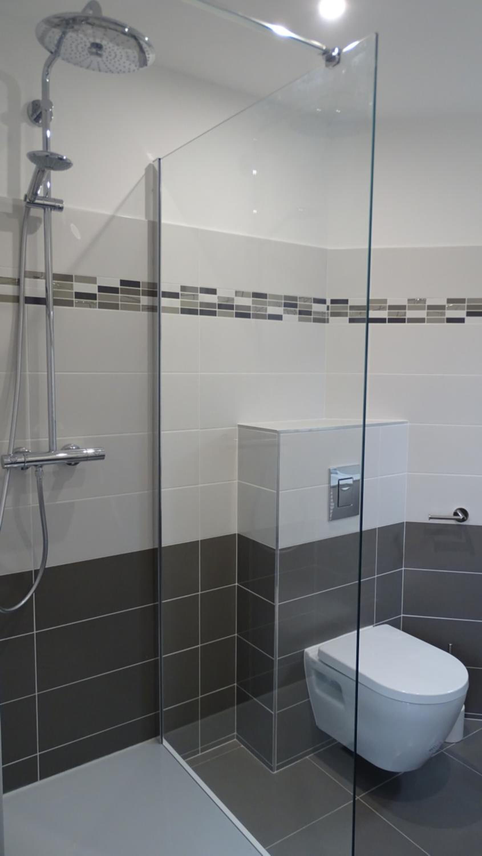 A modern bathroom with a glass-enclosed shower, a toilet, and a tiled floor.