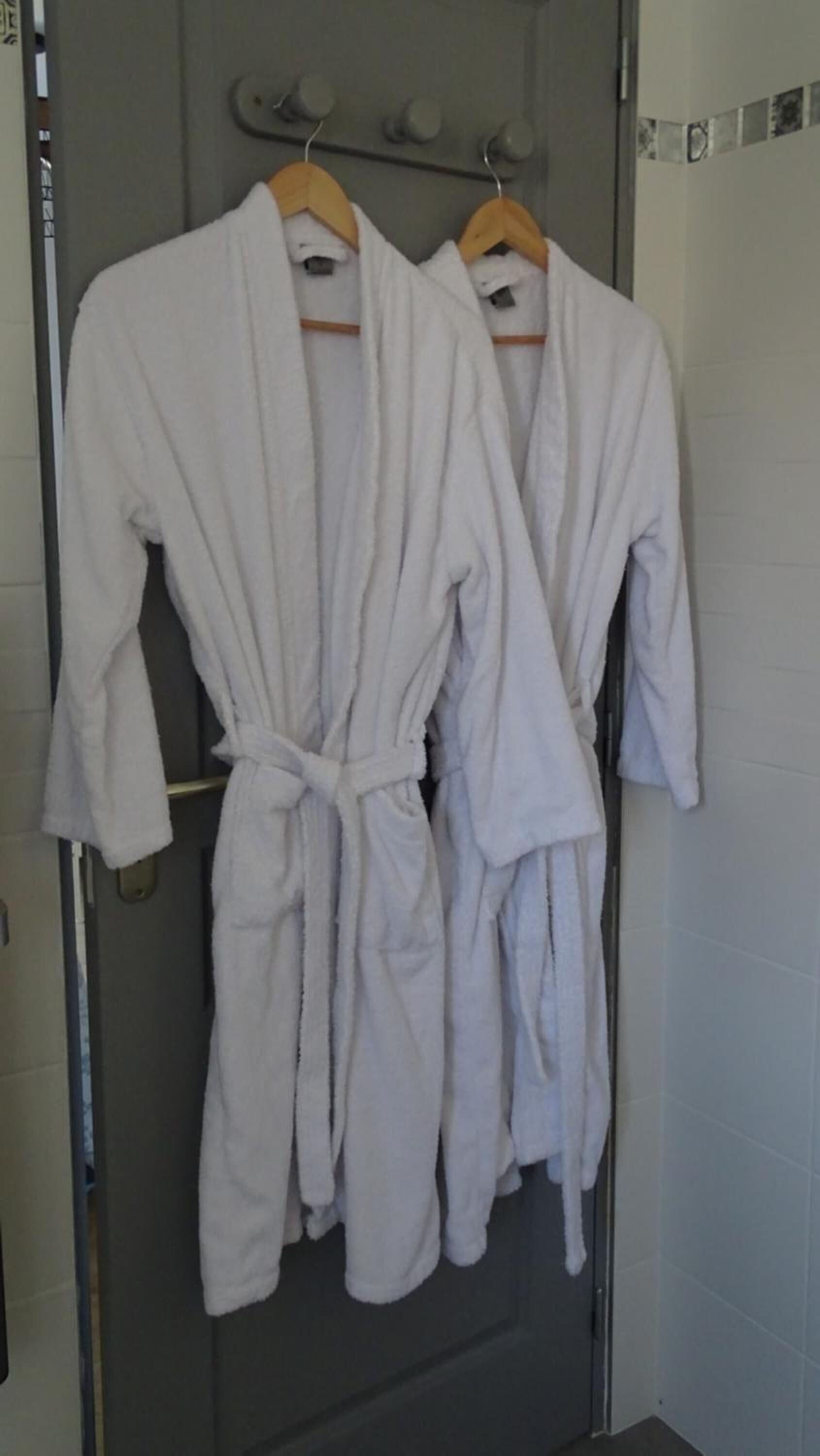 Two white bathrobes hanging on a rack in a bathroom.