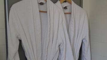 Two white bathrobes hanging on a rack in a bathroom.