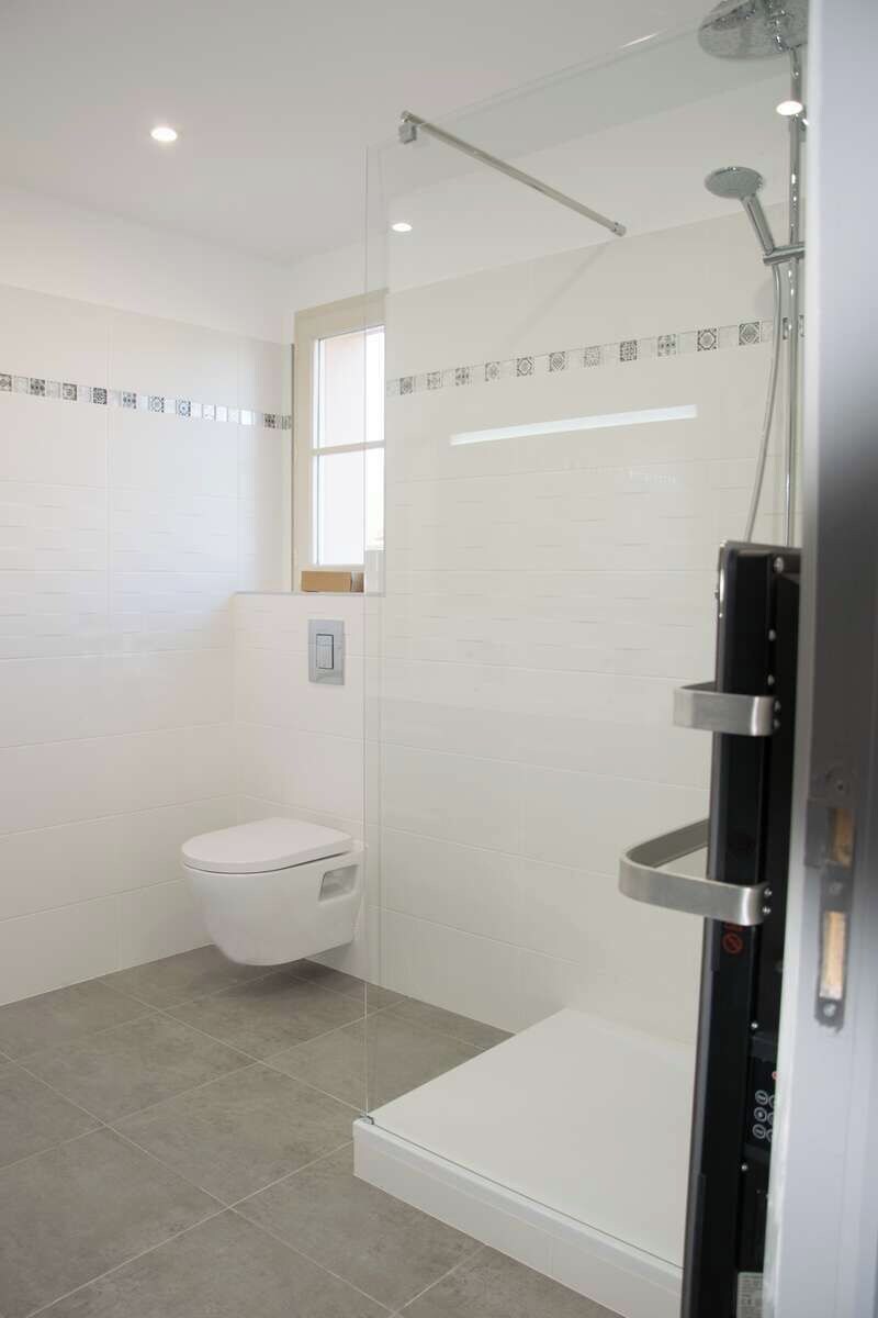 Ein modernes Badezimmer mit einer gläsernen Dusche, einer weißen Toilette und einem gefliesten Boden.