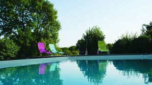 Una piscina con acqua limpida che riflette alberi e alcuni lettini colorati.