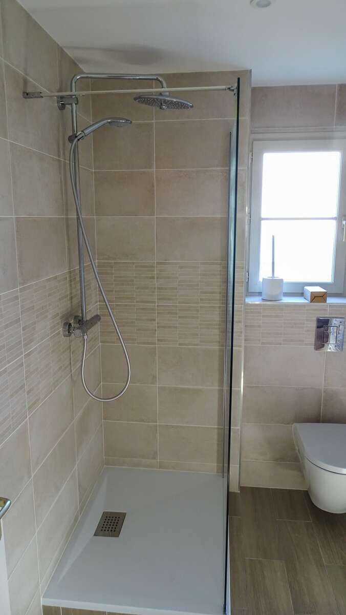 A shower area with a glass door, a handheld showerhead, and a wall-mounted faucet.