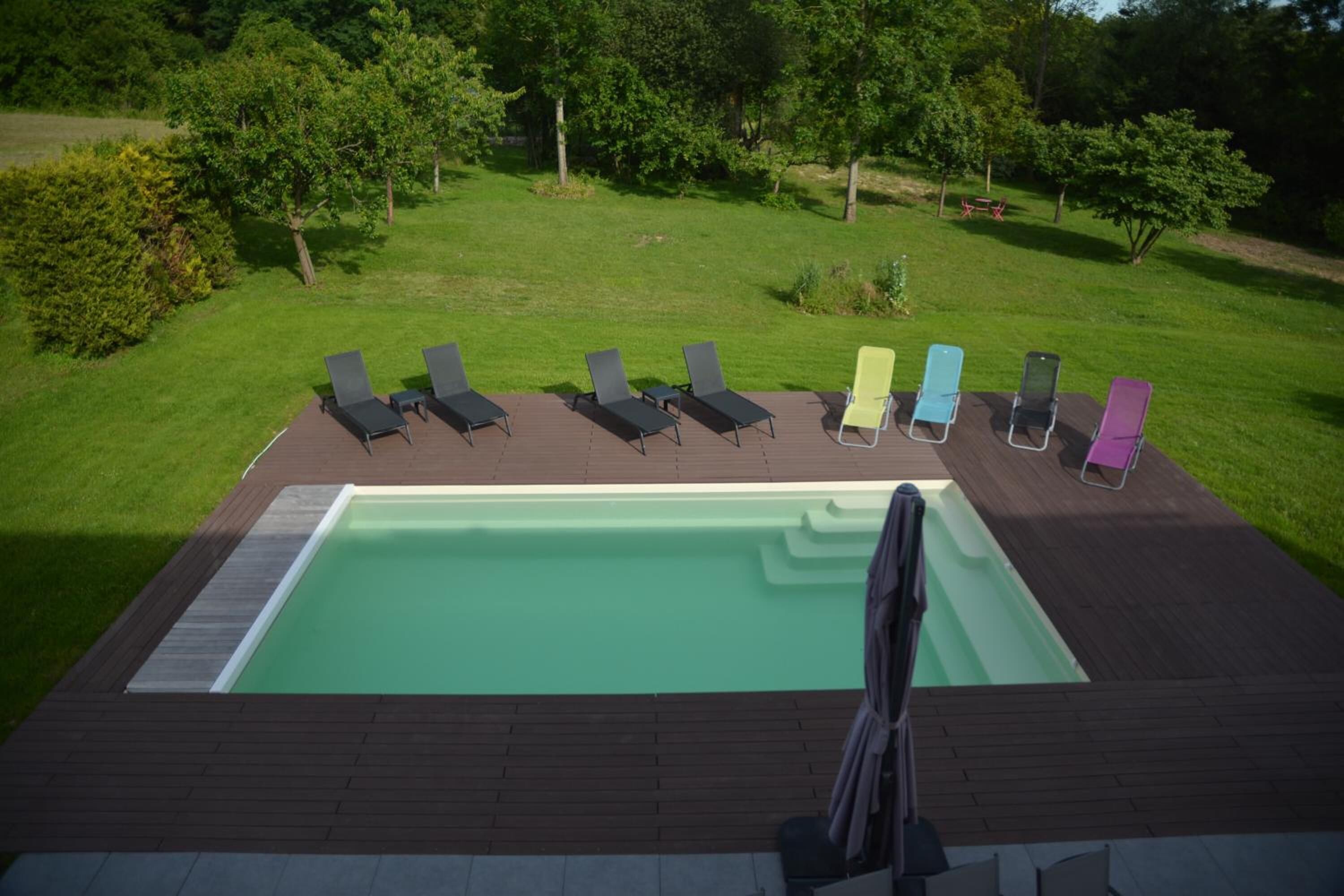 Une piscine rectangulaire dotée d’une terrasse en bois et de chaises longues.