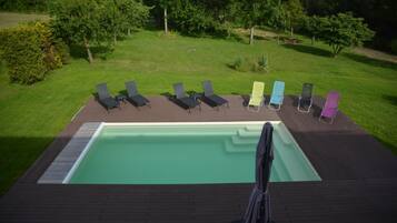 Une piscine rectangulaire dotée d’une terrasse en bois et de chaises longues.