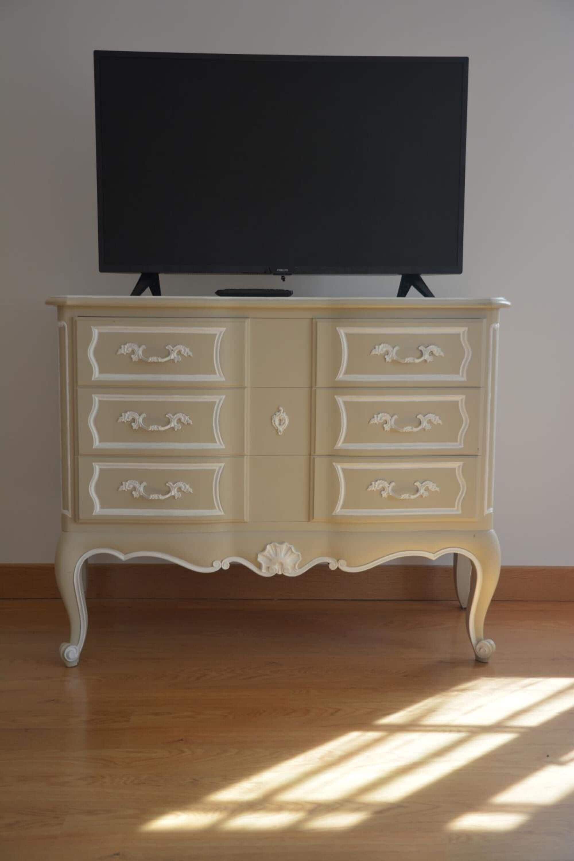 A beige dresser with ornate handles and a flat-screen TV on top.