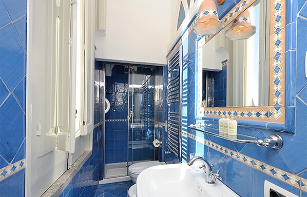 A bathroom with blue tiles, a white sink, and a glass shower enclosure.