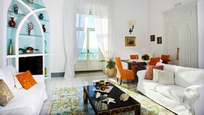 Ein Wohnzimmer mit einem weißen Sofa, einer Glastrennwand, einem Couchtisch und Meerblick durch ein Fenster.