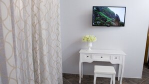 A white desk with a vase of flowers, a television mounted on the wall, and a patterned curtain. - Reginella B&B Palermo (Palermo)