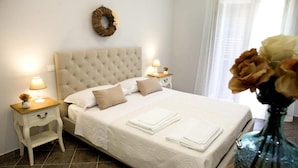 A neatly made bed with white linens, two bedside tables with lamps, a vase with flowers, and a wall-mounted wreath. - Reginella B&B Palermo (Palermo)