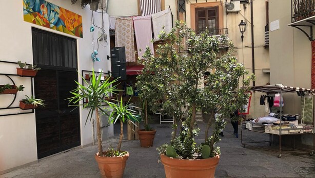 A narrow street with potted plants, a market stall, and a building with a colorful mural. - Reginella B&B Palermo (Palermo)