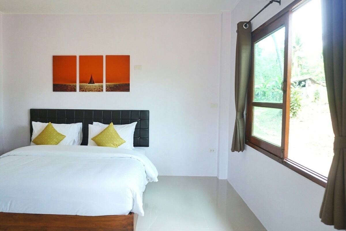 A bedroom with a bed, a headboard, a window with curtains, and a wall with three orange paintings.