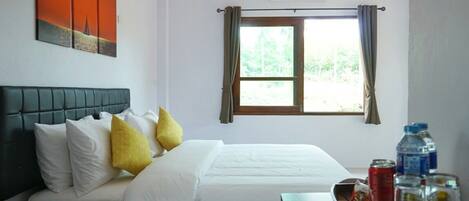 Una habitación de hotel con cama, ventana con cortinas, aire acondicionado instalado en la pared y un atril con agua embotellada y aperitivos.