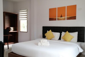 A neatly made bed with white linens and two yellow pillows, a wooden wardrobe, and a window with blinds. - The Lodge at Koh Kood (Ko Kood)