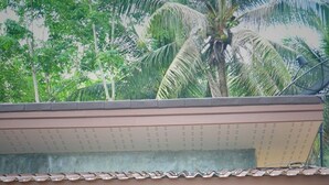 Un pequeño edificio de una sola planta con un porche, dos sillas de madera, una mesita y una cama visible a través de una puerta de vidrio.
