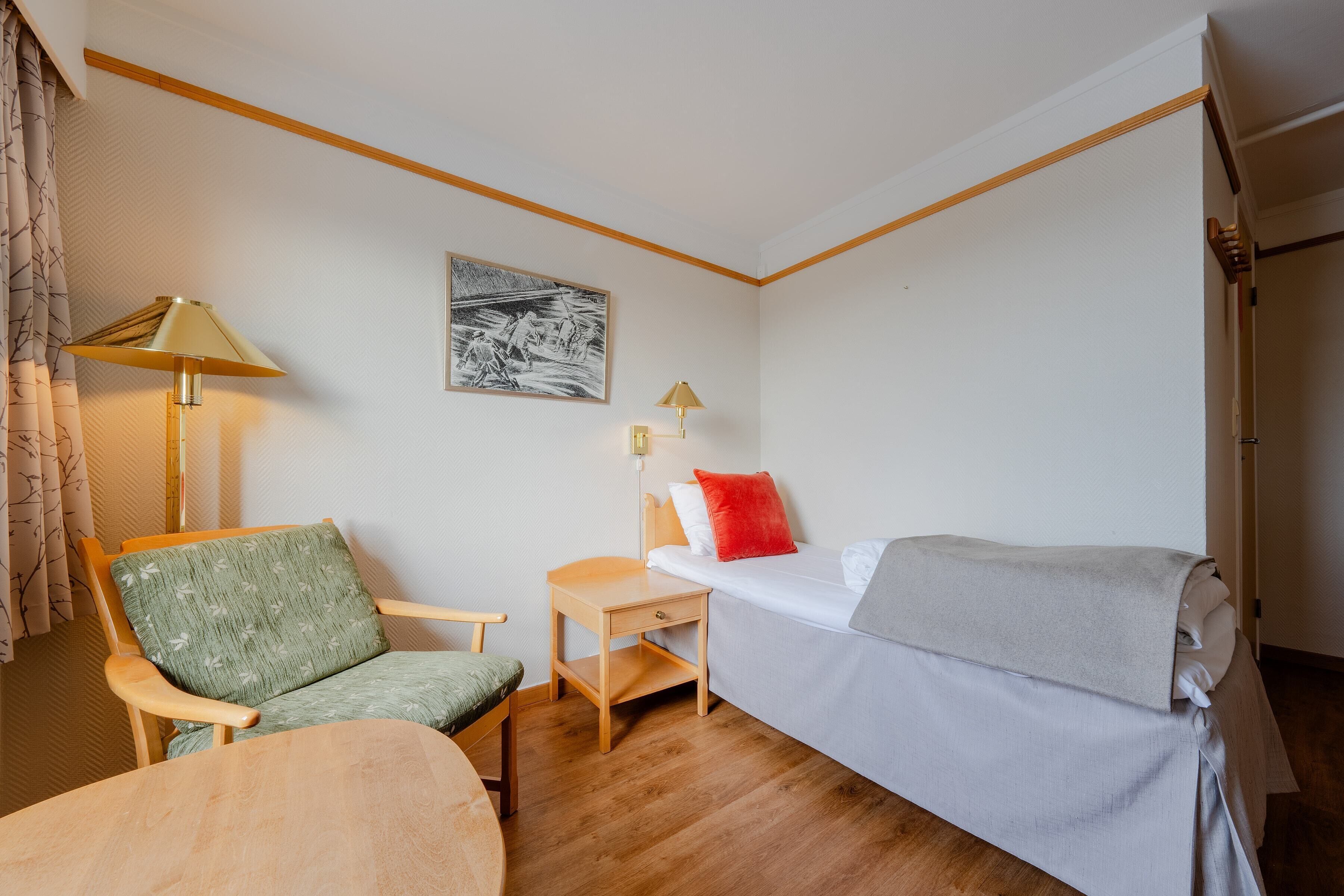 Una habitación pequeña y ordenada con una cama, una silla, una mesa y una lámpara.