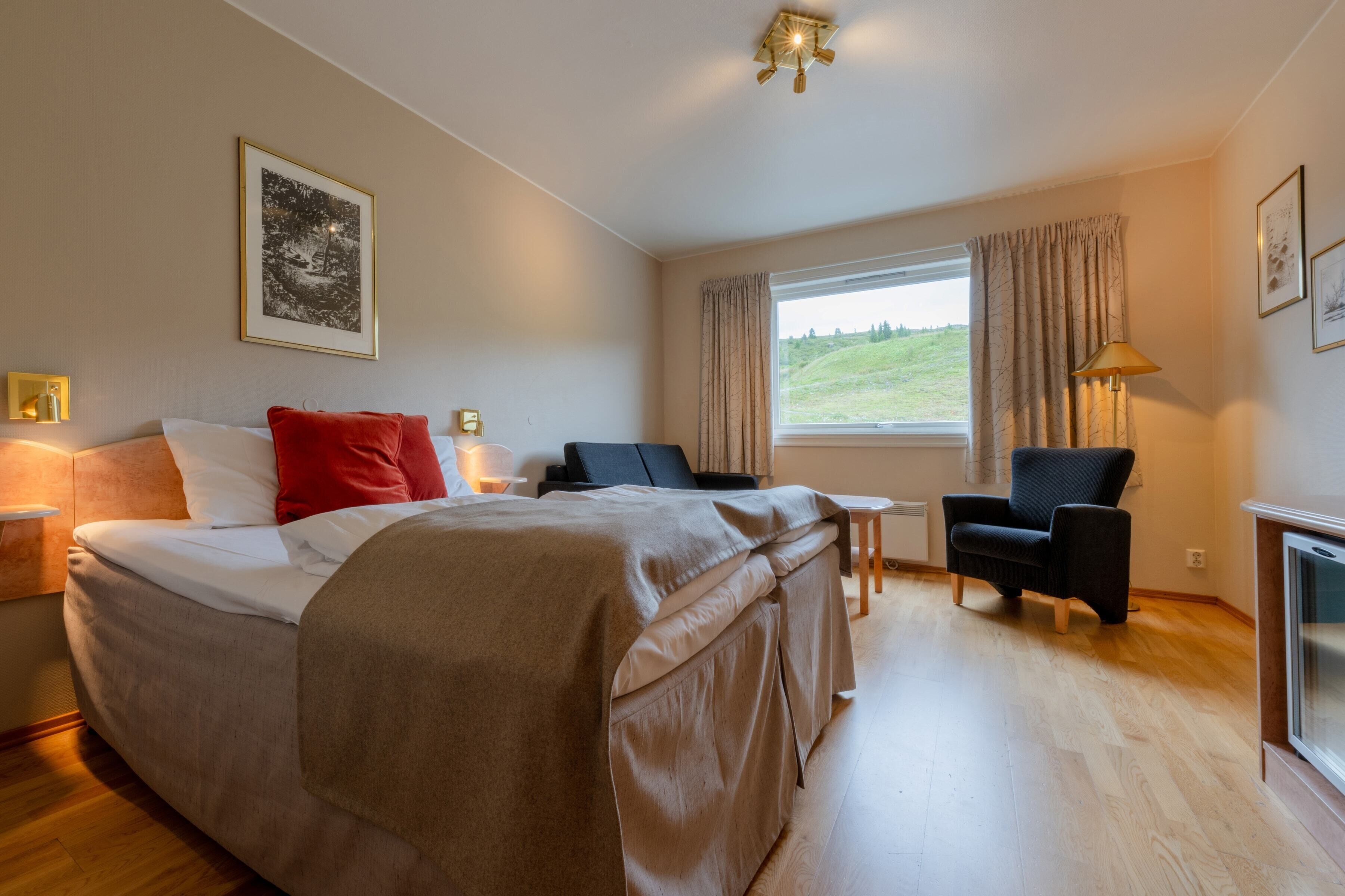 Une chambre à coucher avec un grand lit, une chaise, une petite table et une fenêtre donnant sur un paysage verdoyant.