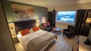 A hotel room with a large bed, a sofa, a chair, a small table, and a view of a snowy landscape through the window. - Storefjell Resort Hotel (Gol)