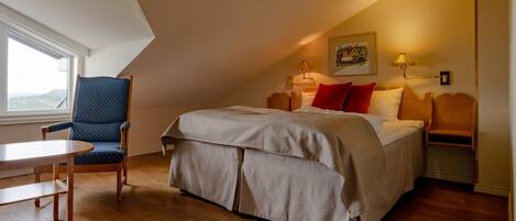 A bedroom with a bed, a chair, a table, and a window.