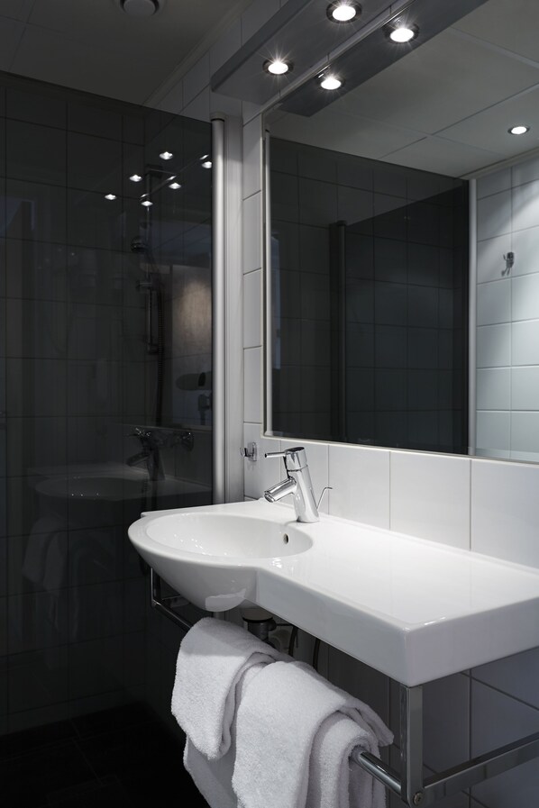 Un baño moderno con ducha acristalada, un lavamanos blanco y un espejo grande.