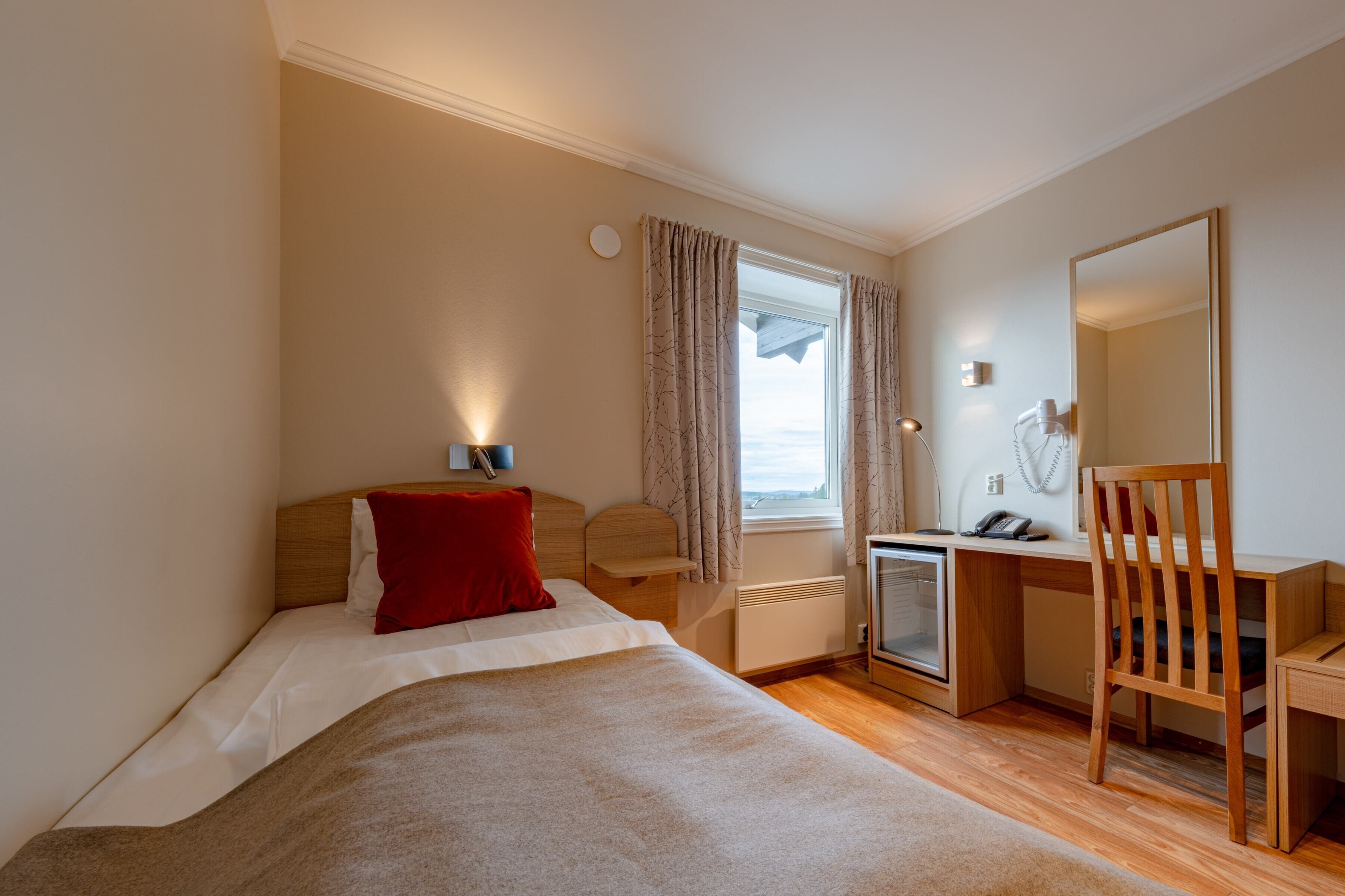 Un dormitorio con cama, escritorio, silla, ventana con cortinas y radiador.