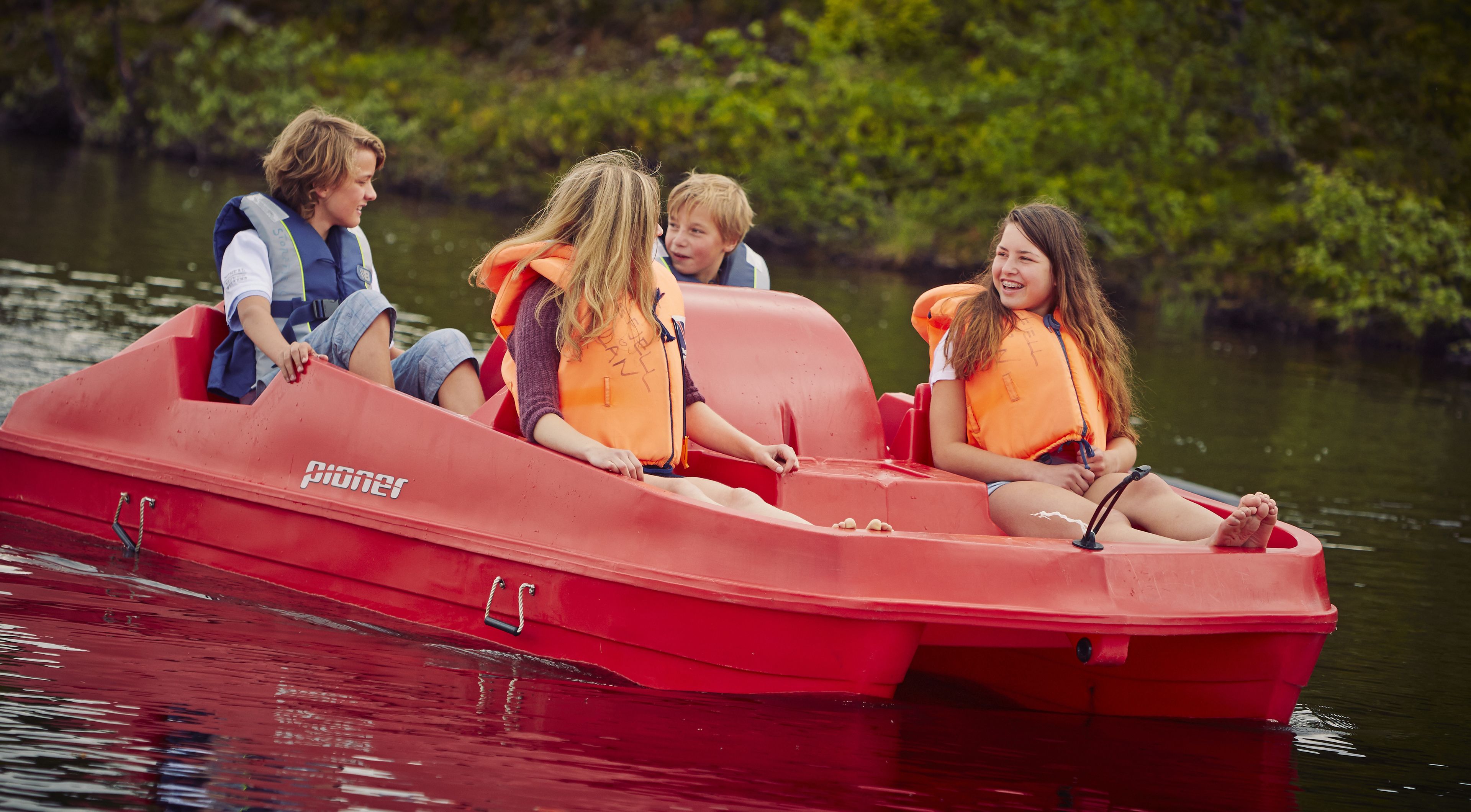 A red boat with four people wearing life jackets, floating on calm water.
