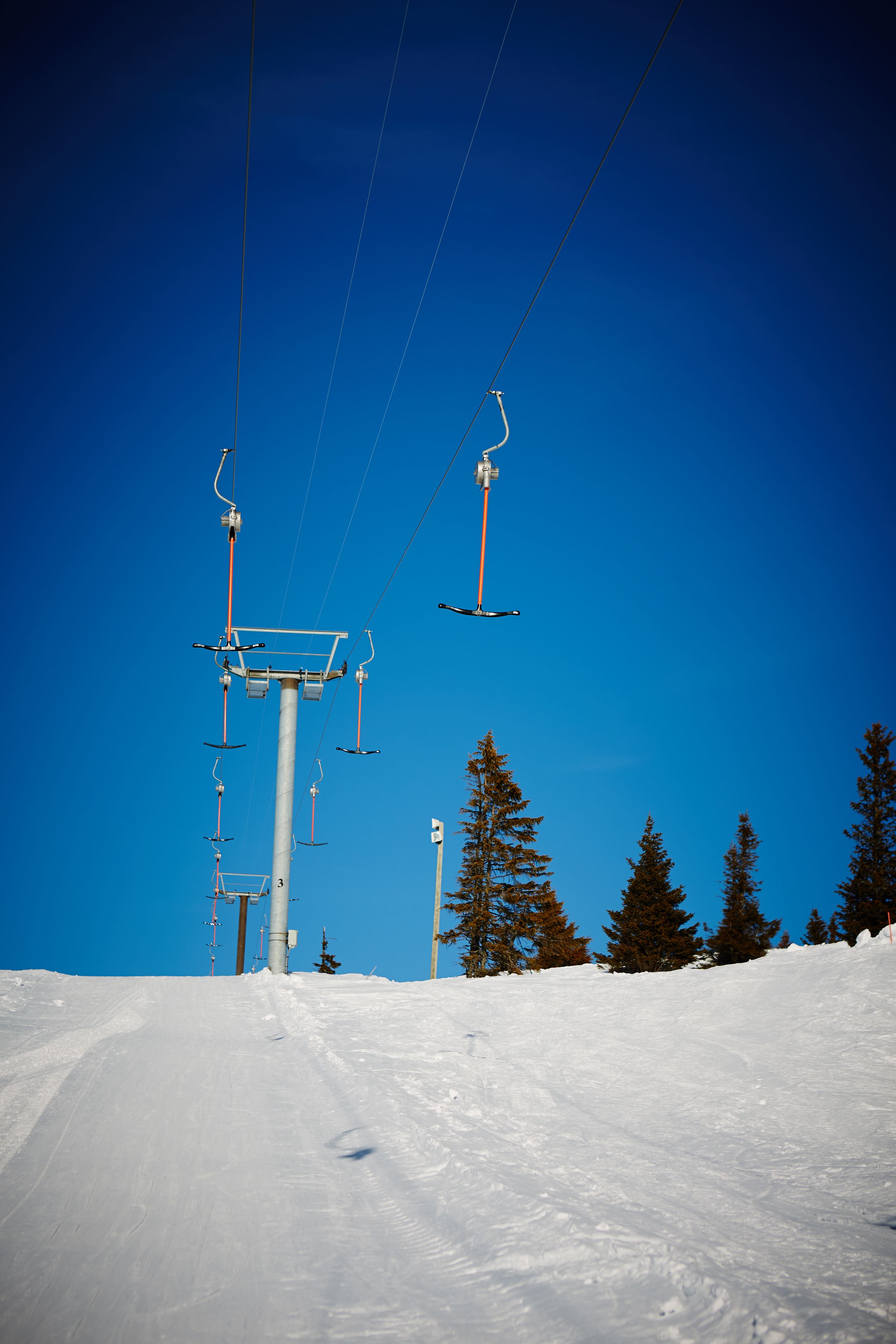 A ski lift with chairs suspended from cables against a clear blue sky.