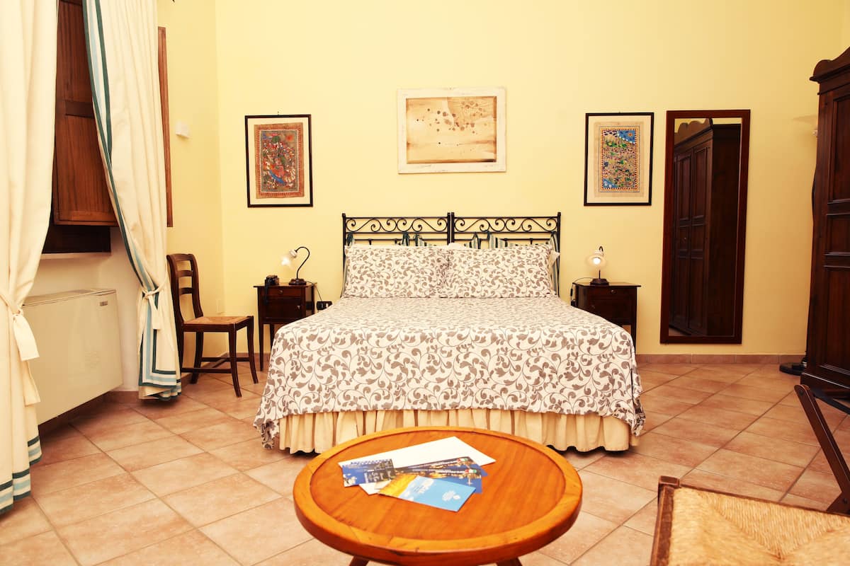 A bedroom with a bed, a chair, a table with papers, and a door.