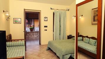 Een slaapkamer met een bed, een stoel, een televisietoestel, een stenen muur en een balkon met planten.