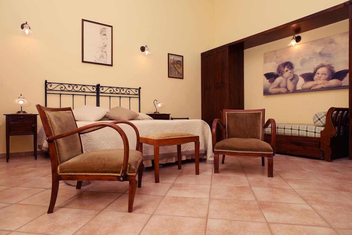 A bedroom with a bed, two nightstands, two chairs, and a painting on the wall.