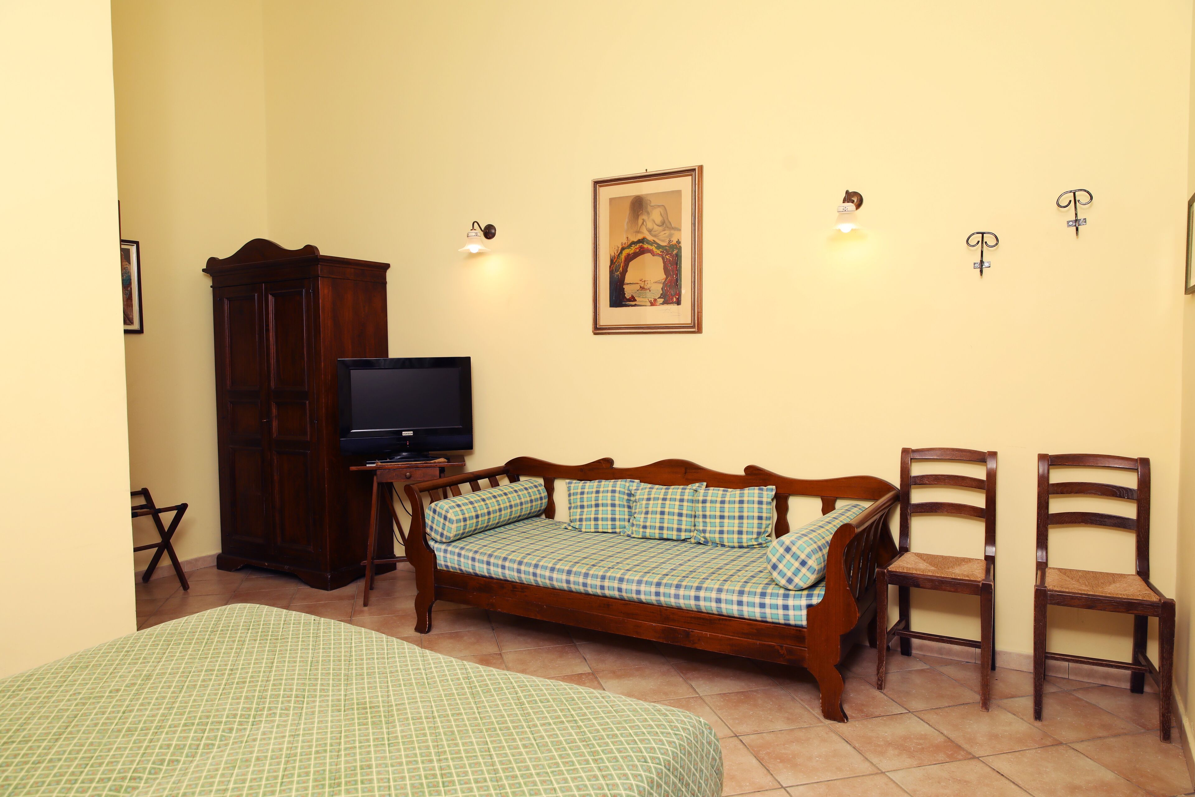 A room with a wooden sofa, two wooden chairs, a television, and a framed picture on the wall.