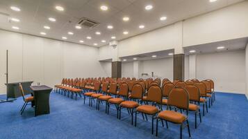 Un salón de conferencias con filas de sillas, un atril y suelo alfombrado.