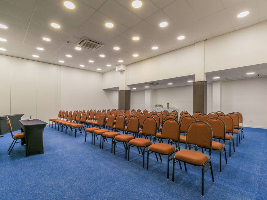 A conference room with rows of chairs, a podium, and a carpeted floor.